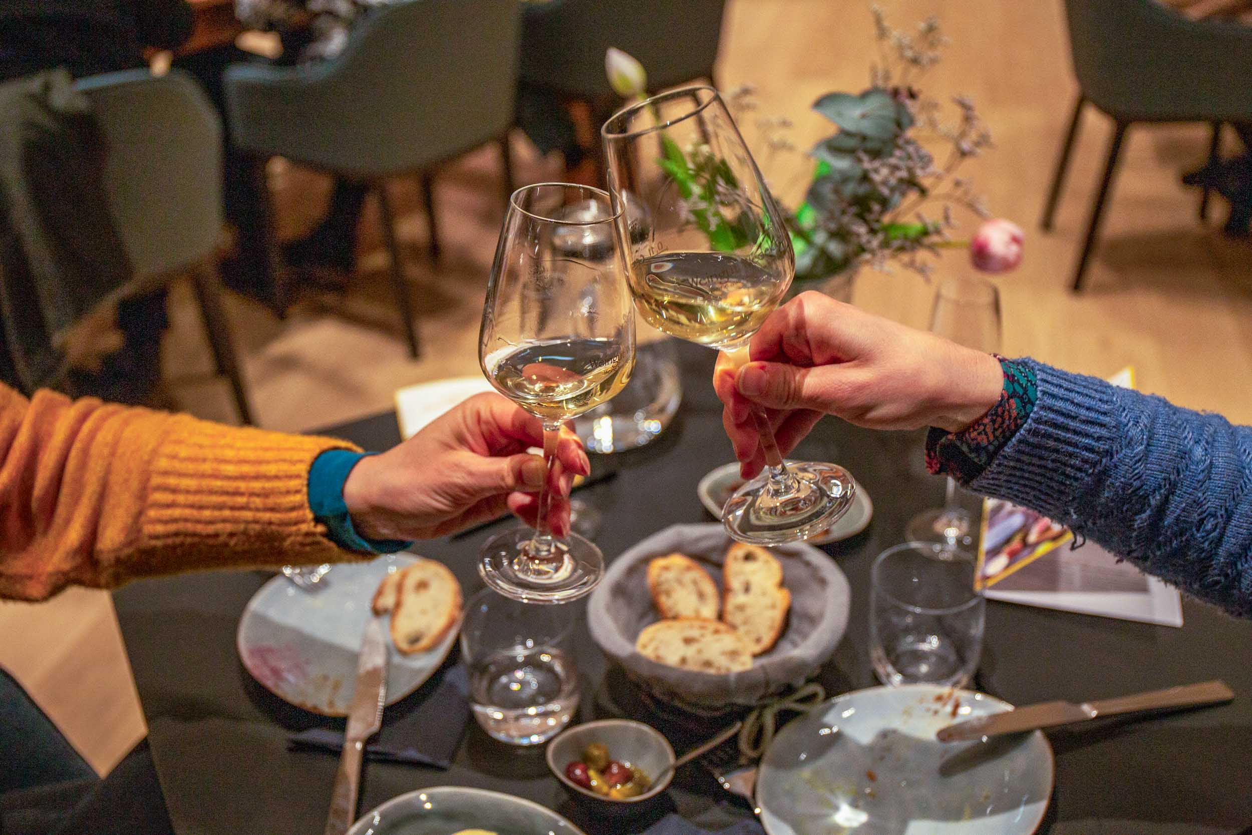 Wein- und Wassergläser stehen auf einem dunklen Tisch. Daneben ein Schälchen Oliven, ein Schälchen Feigen-Chutney und ein Brotkorb mit geschnittenem Baguette.