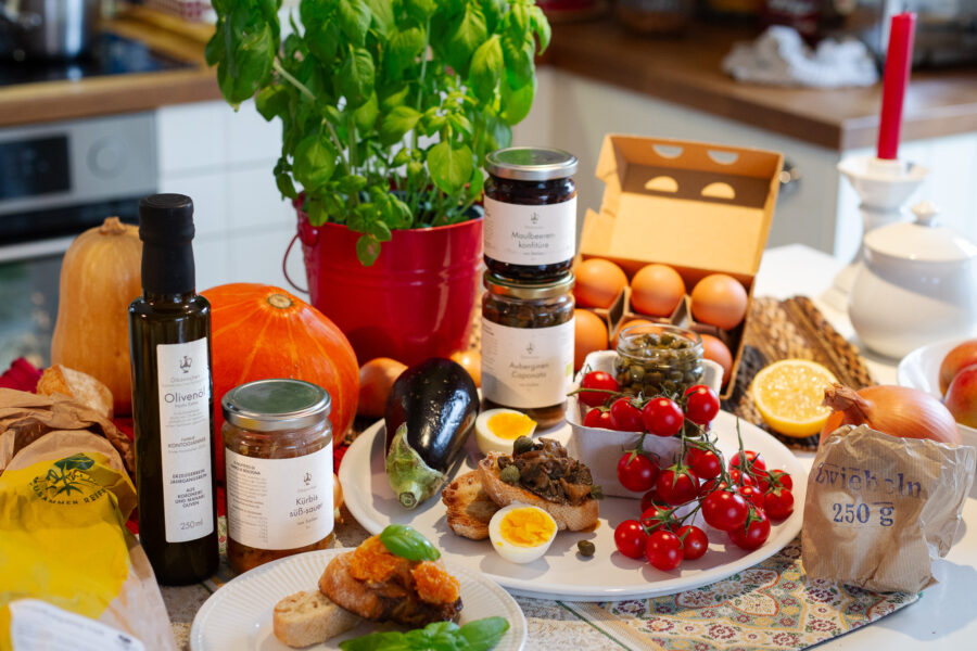 Feinkost-Antipasti aus Sizilien von Ölkännchen online kaufen: Süß-saurer Kürbis, Auberginen-Caponata, Maulbeerenkonfitüre und hochwertiges Olivenöl, serviert mit Weißbrot und Zwiebeln. Hergestellt aus frischen, regionalen Bio-Lebensmitteln wie Basilikum, Auberginen, Kürbis, Tomaten, Eiern und Kapern. Mediterrane Delikatessen – ideal als Antipasti, Geschenkset oder zum Servieren für Gäste und Freunde zu Hause.