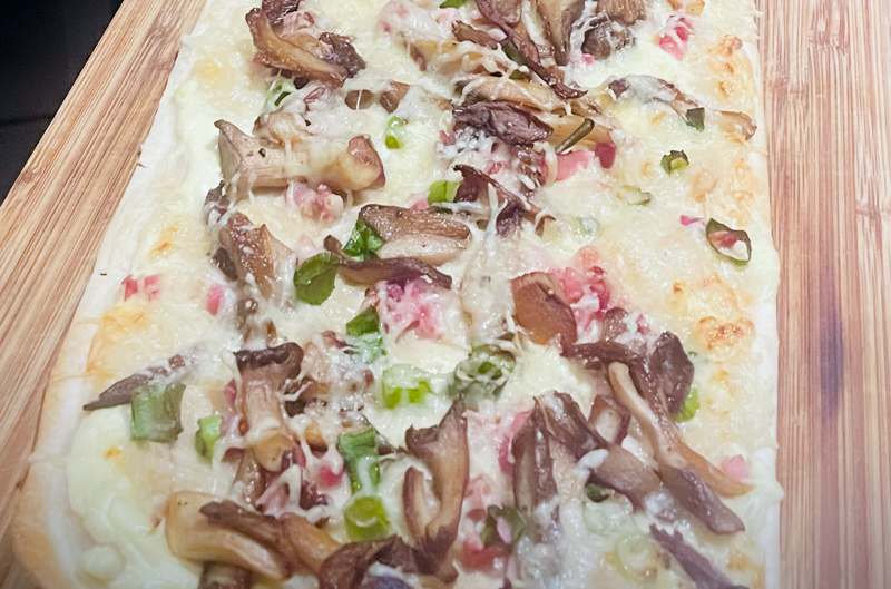 Flammkuchen mit Lauchzwiebeln, Speck und Kräuterseitlingen.