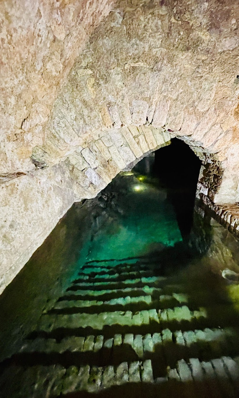 Gemauerter Steinbogen über einer Wasserstelle mit klarem Wasser, das leicht türkisfarben schimmert.