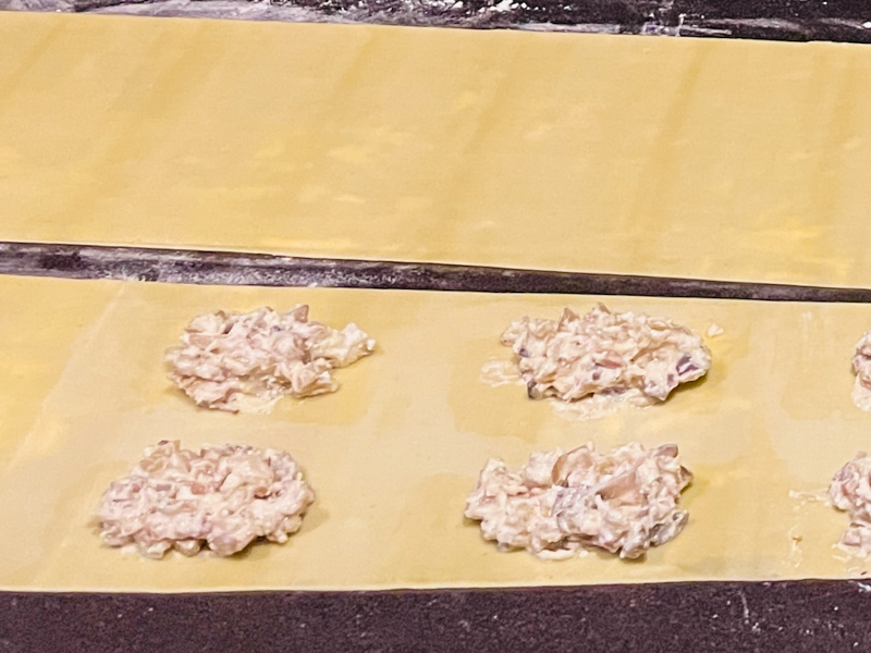 Zubereitungsschritt für „Südtiroler Schlutzkrapfen á la Martina“. Zwei ausgerollte Teigbahnen auf einer bemehlten Fläche. Auf der unteren Teigbahn ist in regelmäßigen Abständen die Pilzfüllung platziert.