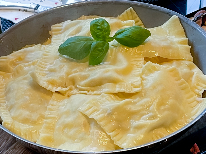 Zubereitungsschritt für „Südtiroler Schlutzkrapfen á la Martina“. Teigtaschen gekocht auf einem Teller angerichtet und mit Basilikum garniert.